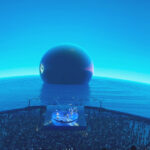 A large blue sphere floating in water next to a shoreline packed with people