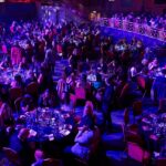 Guests sitting around round tables in blue lighting at the Rise Awards