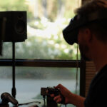 A man wearing a VR headset standing in front of a monitor