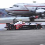 A race car speeding past with an airplane blurred in the background