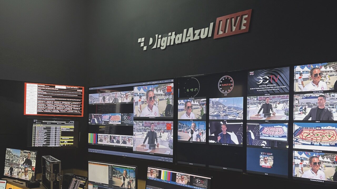 A large wall of monitors showing live streaming with people sitting with laptops next to it