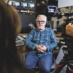 An older man sits in a chair in a studio conducted a filmed interview. Image Darren Robinson Photography