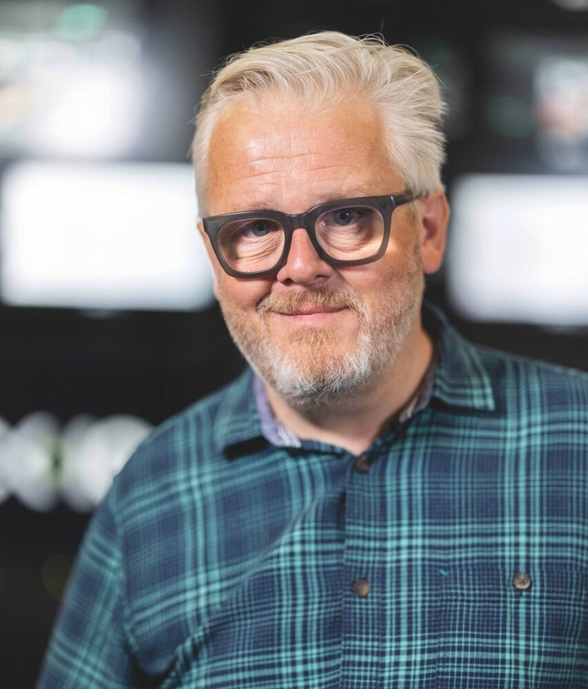 An older man with a beard and black-rimmed glasses with a smile