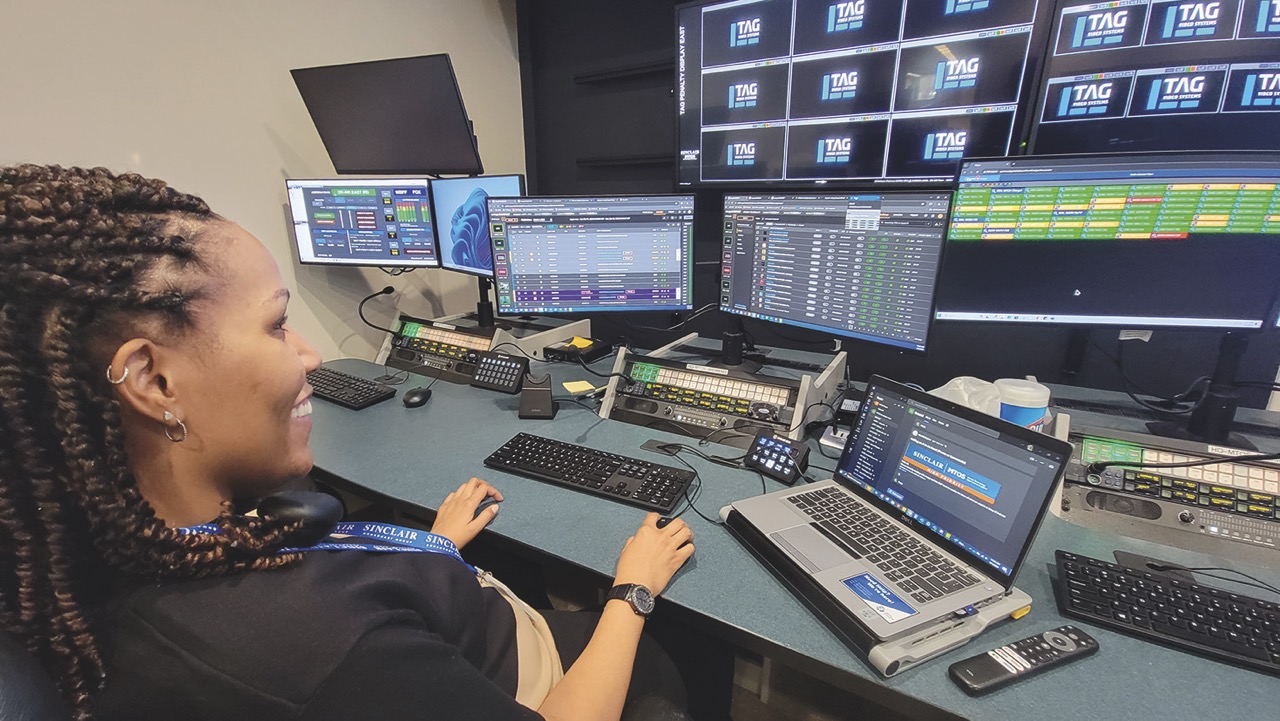 A woman smiling as she works on multiple computer monitors