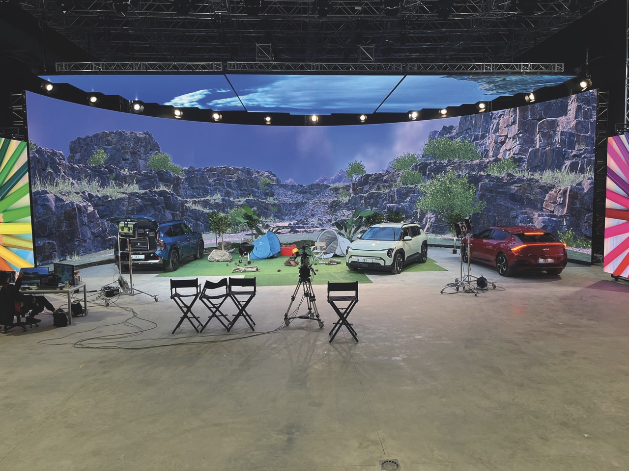 A film set with a large LED screen showing cliffs. Chairs and cars are placed in front of it