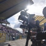 A person and camera in silhouette, filming a stadium filled with people