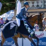 A woman in gear with a helmet riding a horse on grass while a crowd watches behind
