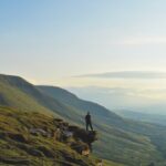 a landscape of hills and sky at sunrise with a person standing in the distance
