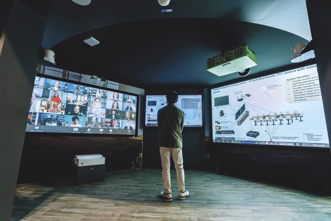 Collab Large A person standing in a room with three large screens on the wall showing different images