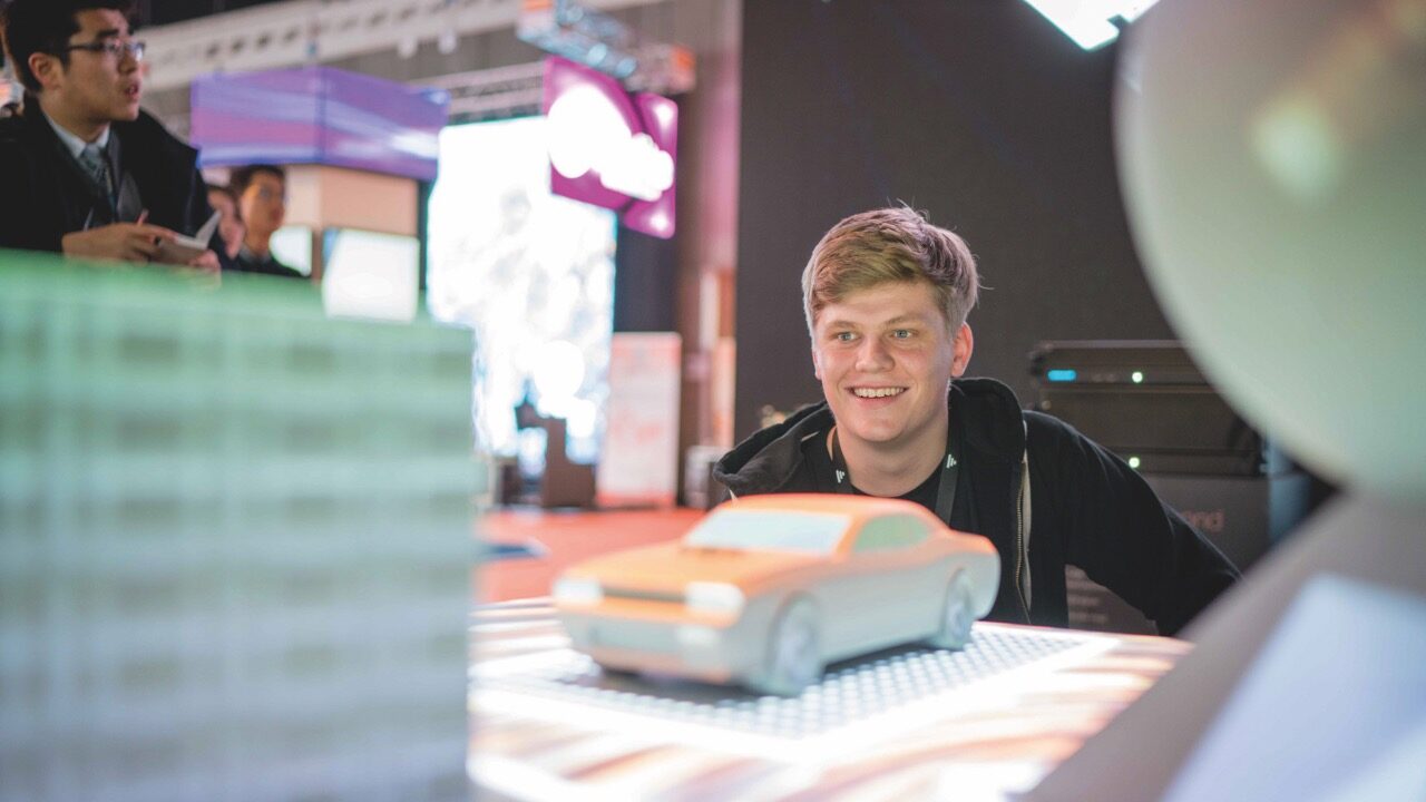 A young man sitting at a table and looking at a model of a car