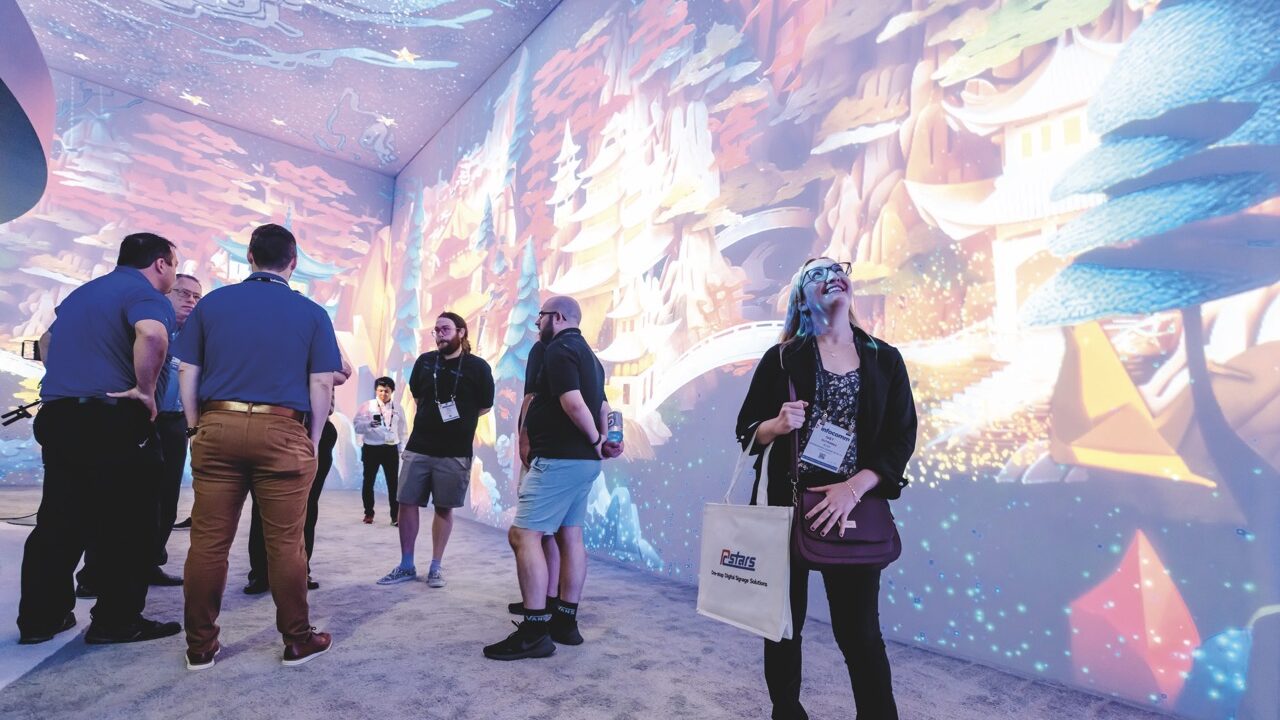 A woman standing and staring up at the ceiling with a smile on her face. She stands in a room with projections on the walls and ceiling with other people