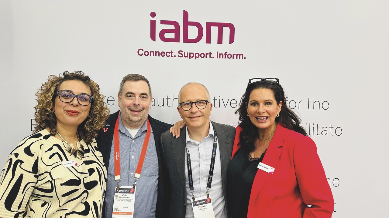 Four people stand in a row with their arms around each other, smiling at the camera