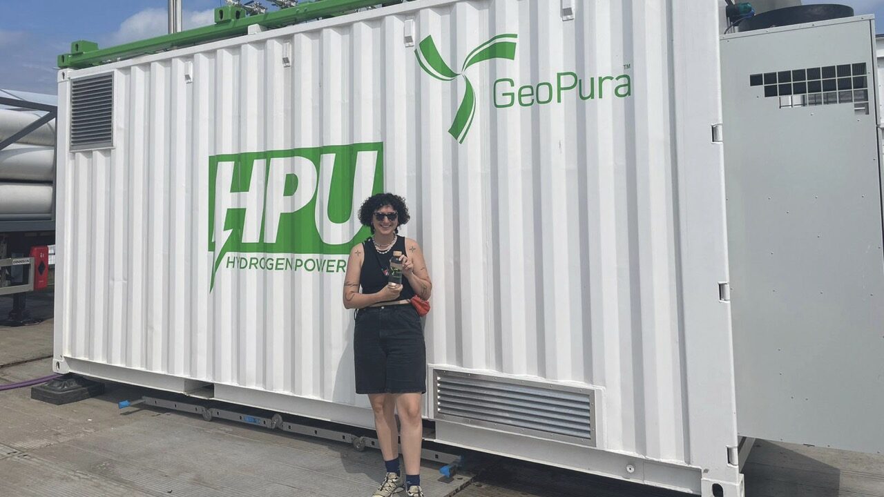 A woman holding a glass bottle and smiling outside a large white container