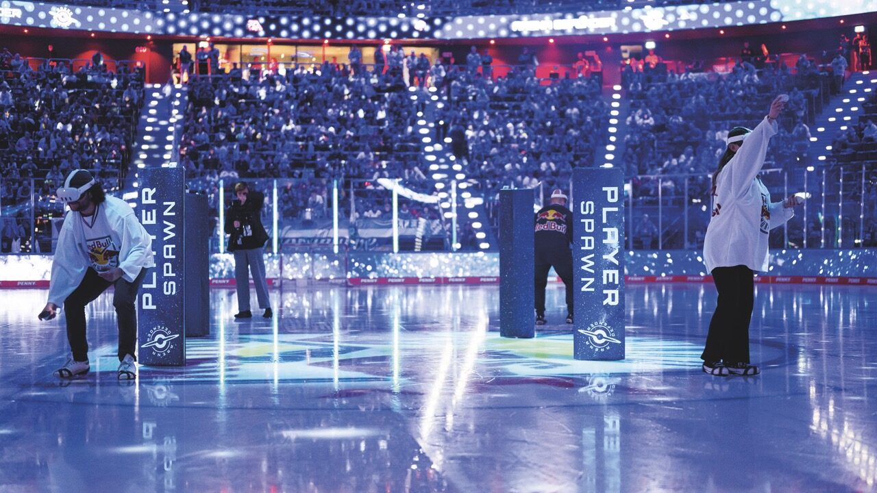 A busy arena with people in the centre using VR headsets. The lighting is dark and blue