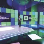 A person stands in a film studio on smooth floors in front of a LED screen background