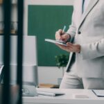 A person standing next to a desk in a suit. They take notes