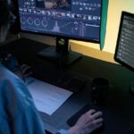 A person working at a dimly lit desk in front of two computers