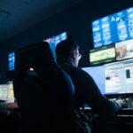 People sitting in large chairs in a dark room, looking at a wall of computer screens